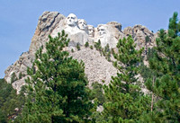 Mount Rushmore se voit de la route entourée de gigantesques rochers. Construit entre 1930 et 1941. -- Mount Rushmore is visible from the highway surrounded by gigantic mountains. Built between 1930 an